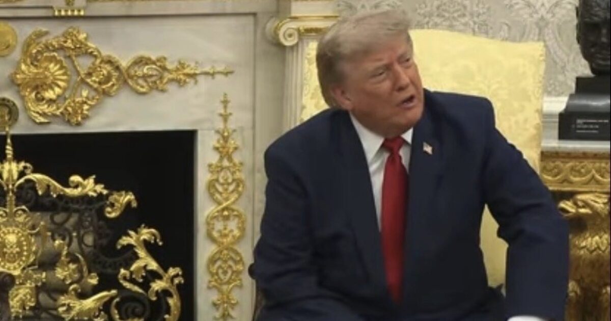 Donald Trump seated in a formal setting, engaging in conversation, with ornate decor and fireplace in the background.