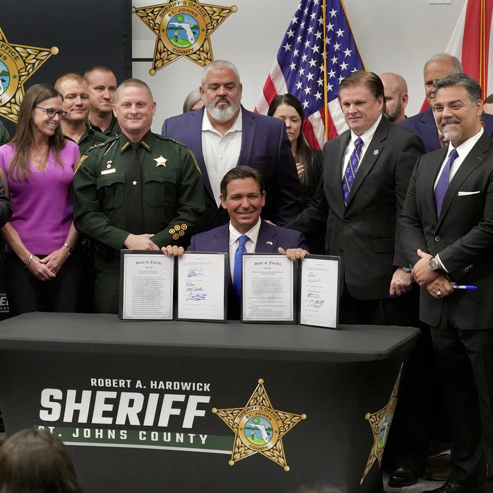 Governor signing legislation with law enforcement officials at St. Johns County Sheriff's Office event, showcasing community collaboration and public safety initiatives.