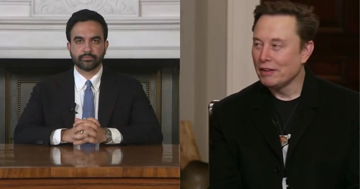 Two men seated at a table, one in a suit and tie, the other in a black jacket, engaged in conversation.