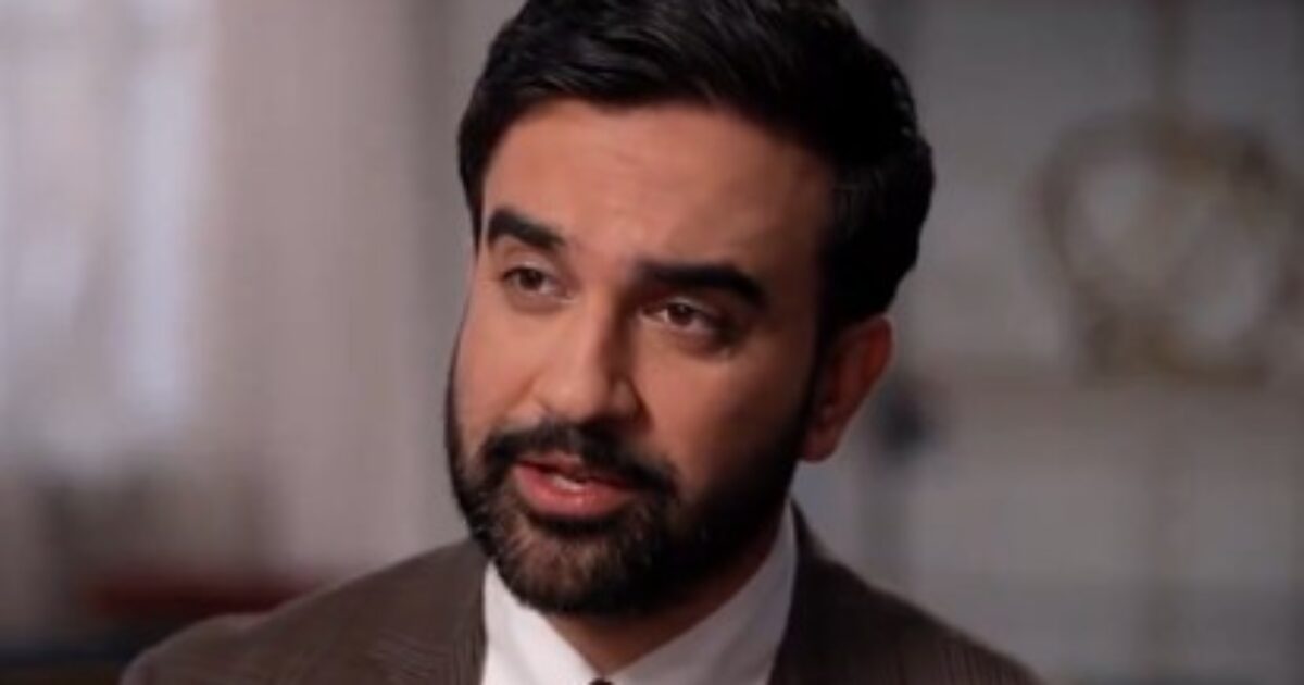 Man with a beard and suit speaking thoughtfully in a well-lit indoor setting, conveying a sense of professionalism and engagement.